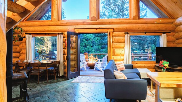 A log cabin interior with a dining area, a living room with a sofa and TV, and a fireplace.