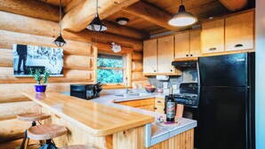 A wooden cabin-style kitchen with a wooden countertop, bar stools, a black refrigerator, and a stove.
