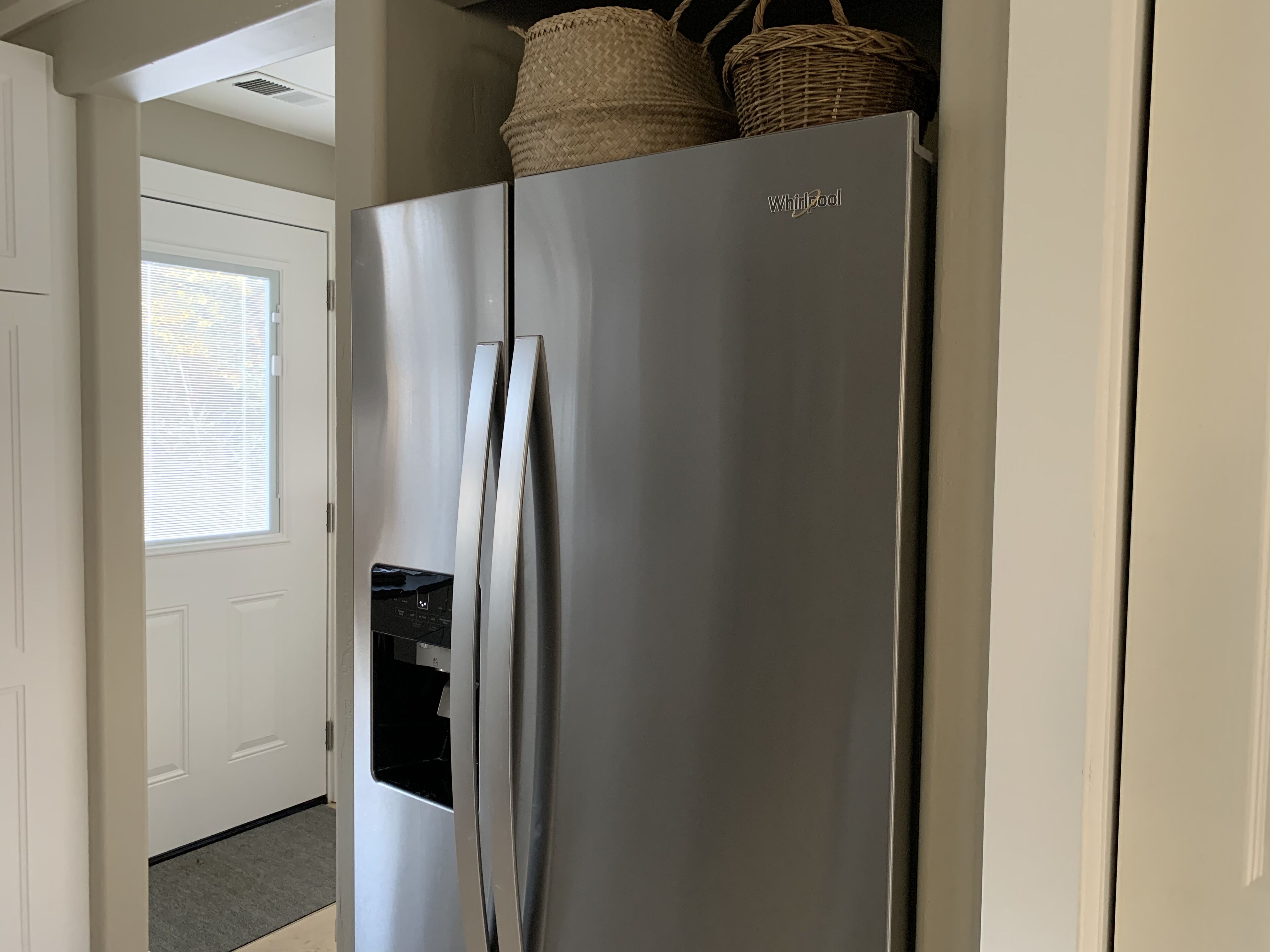 Un refrigerador Whirlpool de acero inoxidable en un pasillo, con una cesta encima.