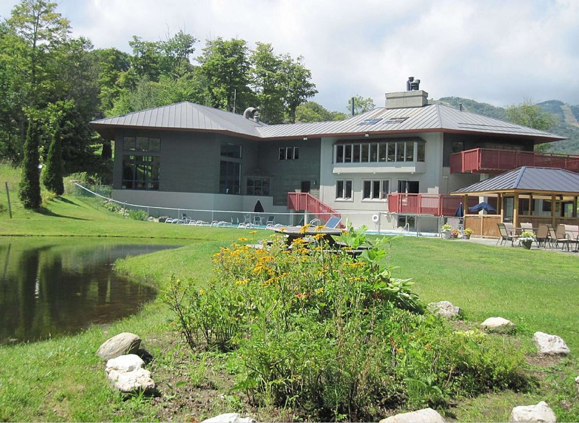 Un bâtiment doté d’une grande fenêtre, d’un espace extérieur abrité avec des sièges et d’un bassin situ é au premier plan.