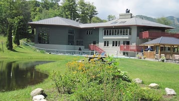 A building with a large window, a covered outdoor seating area, and a pond in the foreground.