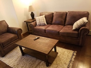 Un salon avec un canapé en cuir marron, un fauteuil assorti, une table basse en bois et une lampe posée sur une table d’appoint.