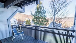 Una terraza de madera con barandilla, una silla y vistas a árboles y casas al fondo.