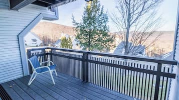 A wooden deck with a railing, a chair, and a view of a tree and houses in the background.