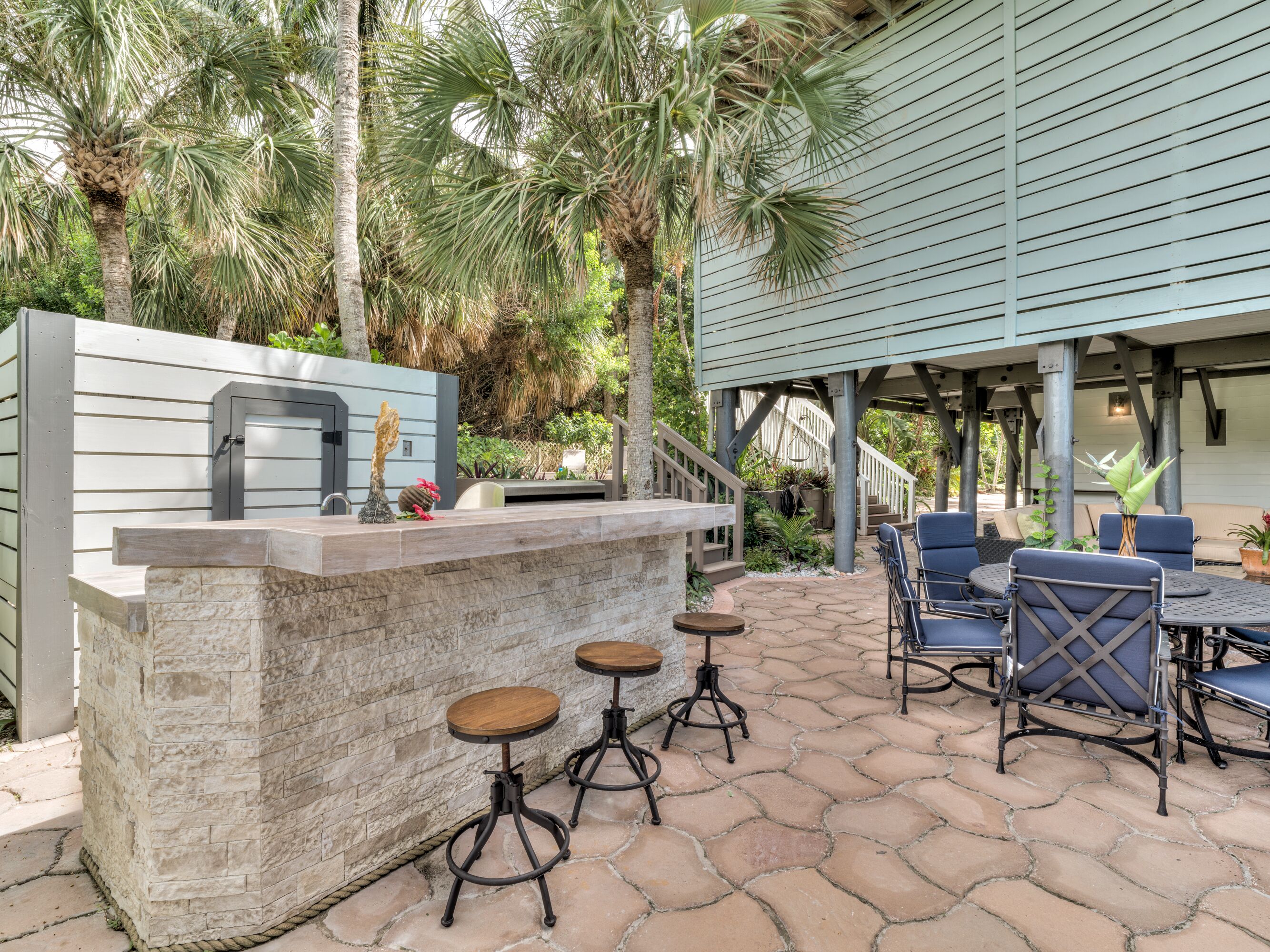 An outdoor patio with a stone bar, seating, and a staircase leading to a covered area.