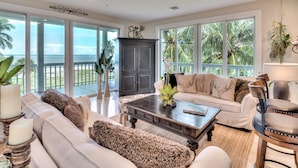 A spacious living room with a large window overlooking the ocean, a dark wooden coffee table, and a white sofa with decorative pillows. - ☀︎🏝⛱︎ Beachfront Elegance⛱︎🏝☀︎  
[2026 Spring + Summer Weeks Available Now!] (North Captiva)
