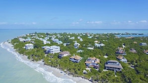 An aerial view of a coastal residential area with houses surrounded by dense greenery and a beach. - ☀︎🏝⛱︎ Beachfront Elegance⛱︎🏝☀︎  
[2026 Spring + Summer Weeks Available Now!] (North Captiva)