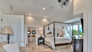 A spacious bedroom with a four-poster bed, a sitting area with a sofa and ottoman, and a view of the outdoors. - ☀︎🏝⛱︎ Beachfront Elegance⛱︎🏝☀︎  
[2026 Spring + Summer Weeks Available Now!] (North Captiva)