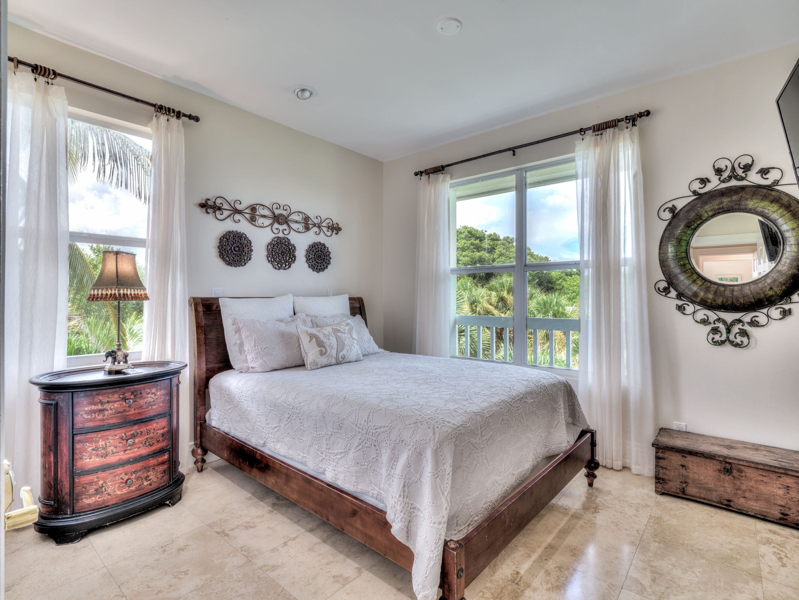 Une chambre avec un grand lit, une table de chevet, un miroir décoratif et une vue sur la verdure.