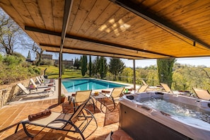 A covered outdoor area with a pool, lounge chairs, and a hot tub.