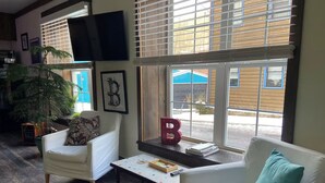 A living room with a white sofa, a white armchair, a coffee table, and a large window with blinds. - Art Studio: Historical Carriage House in the Poconos (Jim Thorpe)