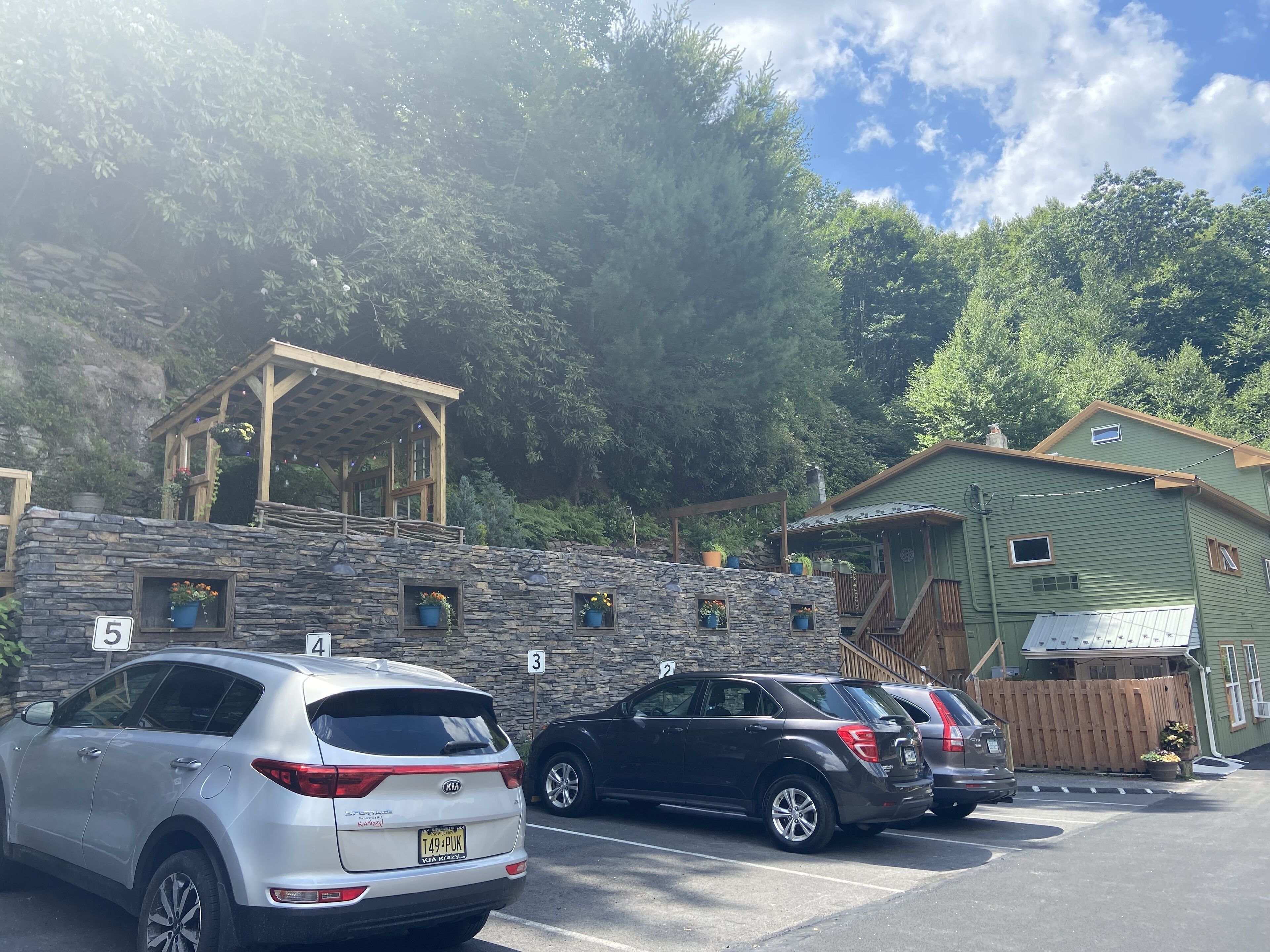 A parking area with cars, a stone wall, and a wooden structure with windows.