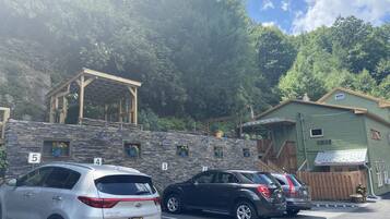 A parking area with cars, a stone wall, and a wooden structure with windows.