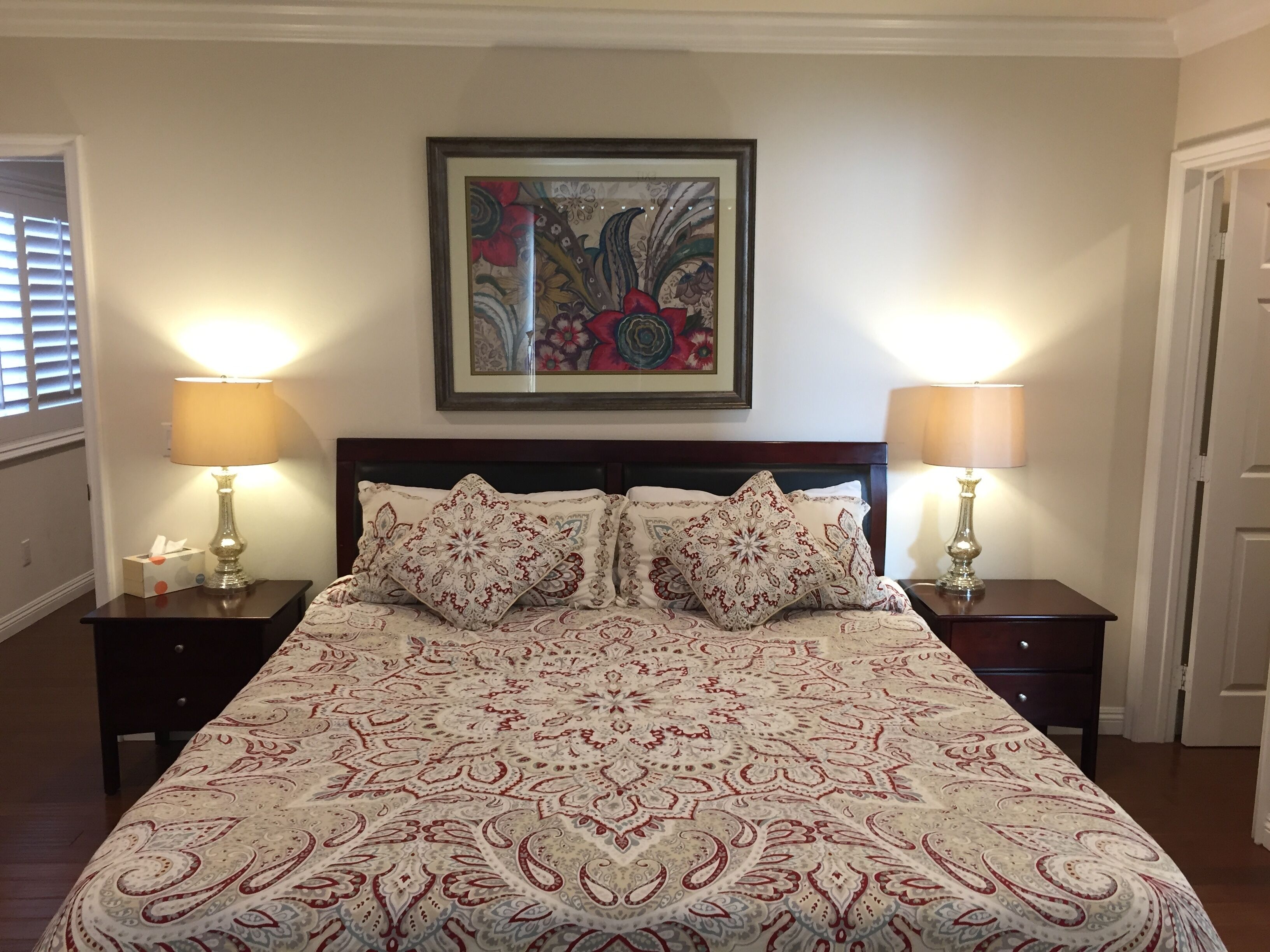 A neatly made bed with patterned bedding, two bedside lamps, and a framed floral artwork on the wall.