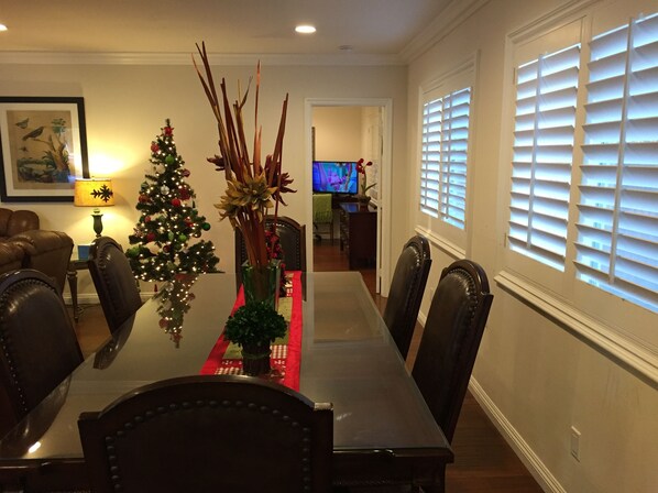 A dining area with a Christmas tree, a vase with flowers, and a television in the background.