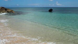 A beach with clear turquoise water, a rocky shoreline, and a small rock formation in the distance. - Beachfront penthouse, Speightstown, stunning West Coast, full AC, near amenities (Speightstown,)
