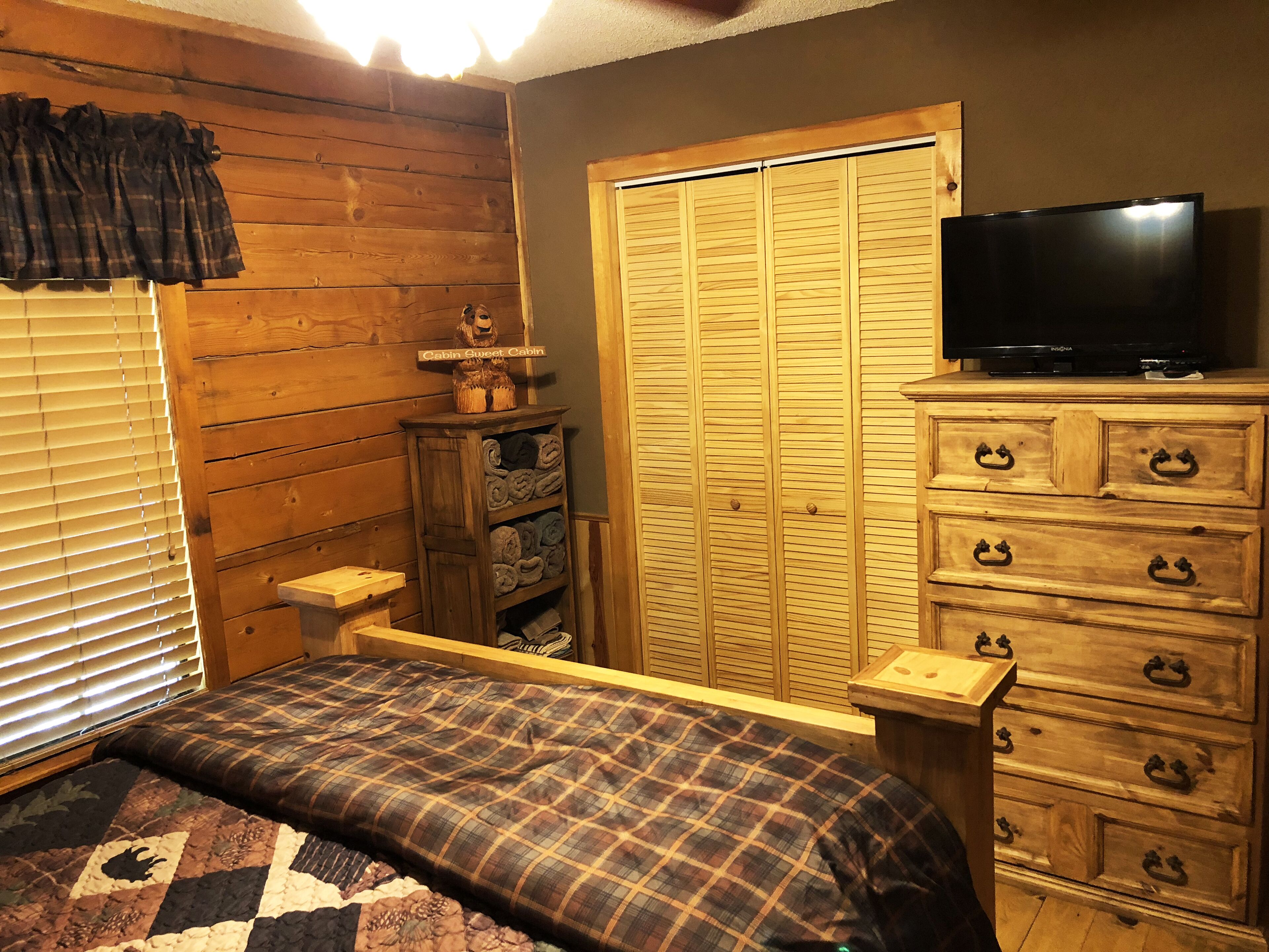 A cozy cabin-style room with a bed, wooden dresser, and a television.