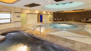 Ein Wellnessbereich mit Whirlpool, Liegestühlen und Bodenfliesen aus Stein.
