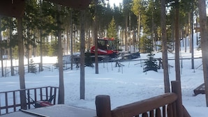 Bosque cubierto de nieve con un quitanieves rojo y una cabaña al fondo.
