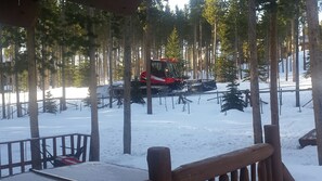 A snow-covered forest with a red snowplow and a cabin in the background.