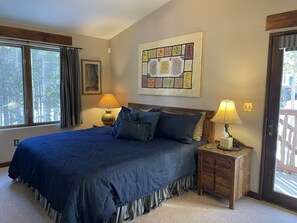 Un dormitorio con una cama grande, dos mesitas de noche con lámparas, un ventanal con cortinas y una pared decorada con una obra de arte colorida.