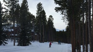 Una pista de esquí nevada con altos pinos y un edificio al fondo.