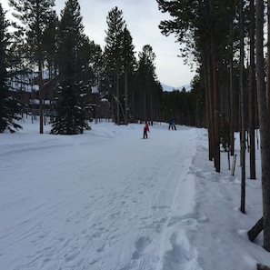 A snowy ski slope with tall pine trees and a building in the background.