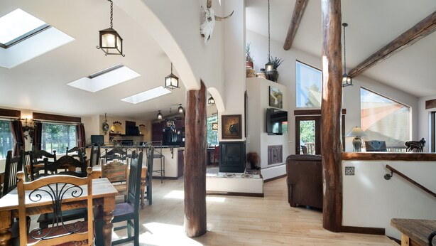 Amplia sala de estar con piso de madera, una mesa de comedor con sillas, una chimenea y un ventanal grande.