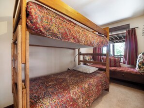A bunk bed with a patterned bedspread, a wooden headboard, and a window with curtains. - SKI IN OUT Perfect for 9 or 19 guests. Above Breckenridge Ski Base Area 8 (Breckenridge)
