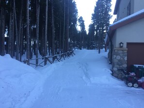 A snow-covered driveway leading to a house with a stone wall and a garage.