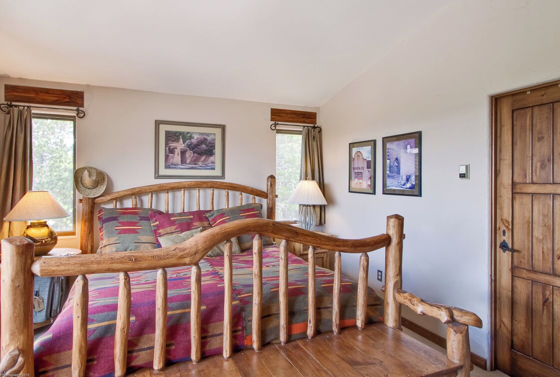 Een bed met houten frame, een kleurrijk beddegoed, twee bedlampjes en fotolijstjes aan de muur.