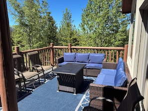 A deck with wicker furniture, a table, and a blue patterned rug.