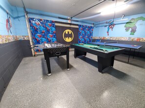Et værelse med et bordtennisbord, et billardbord og en væg med Batman-tema.