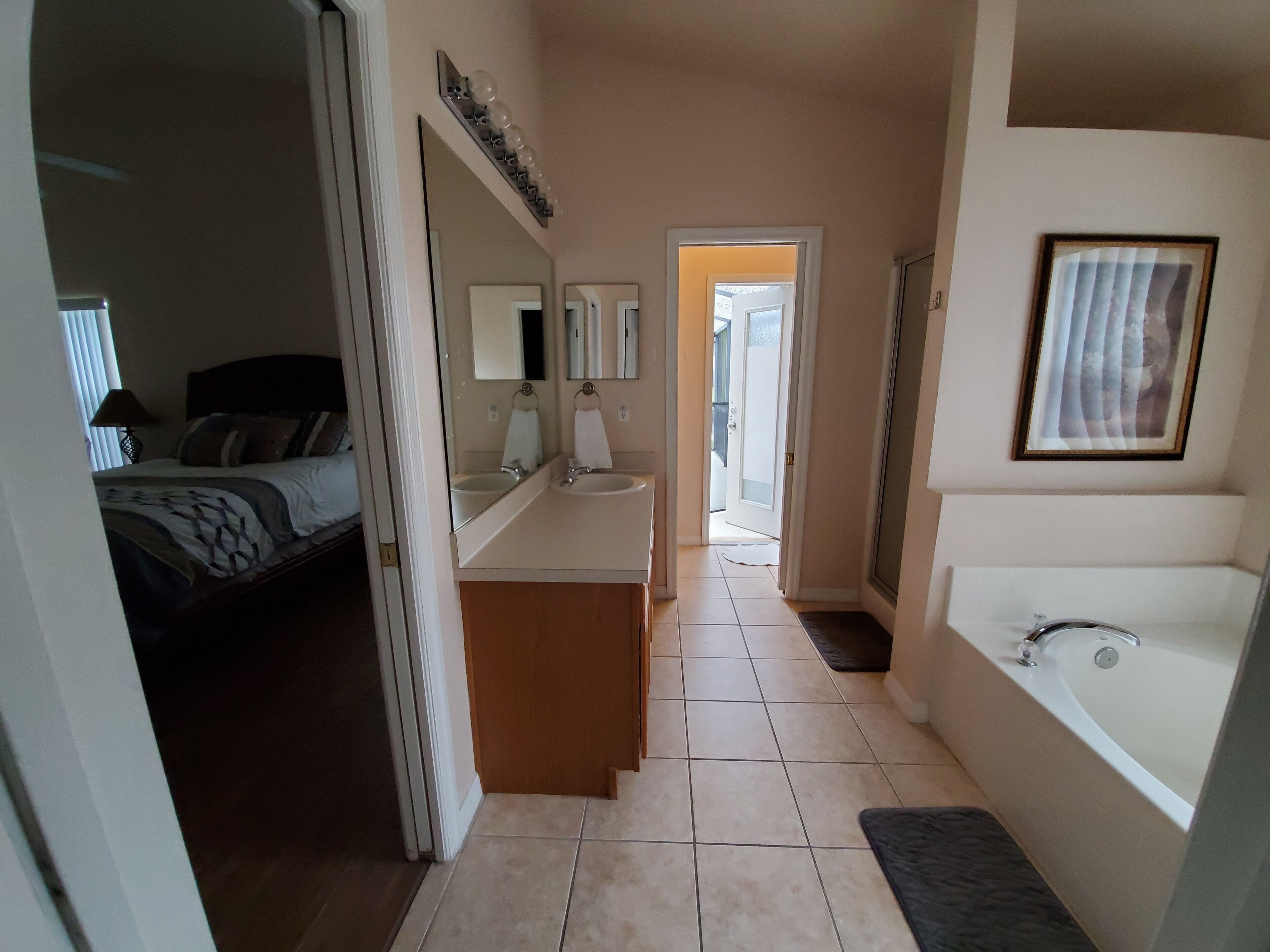 A hotel bathroom with a bathtub, a sink, and a mirror. There is a door leading to another room.