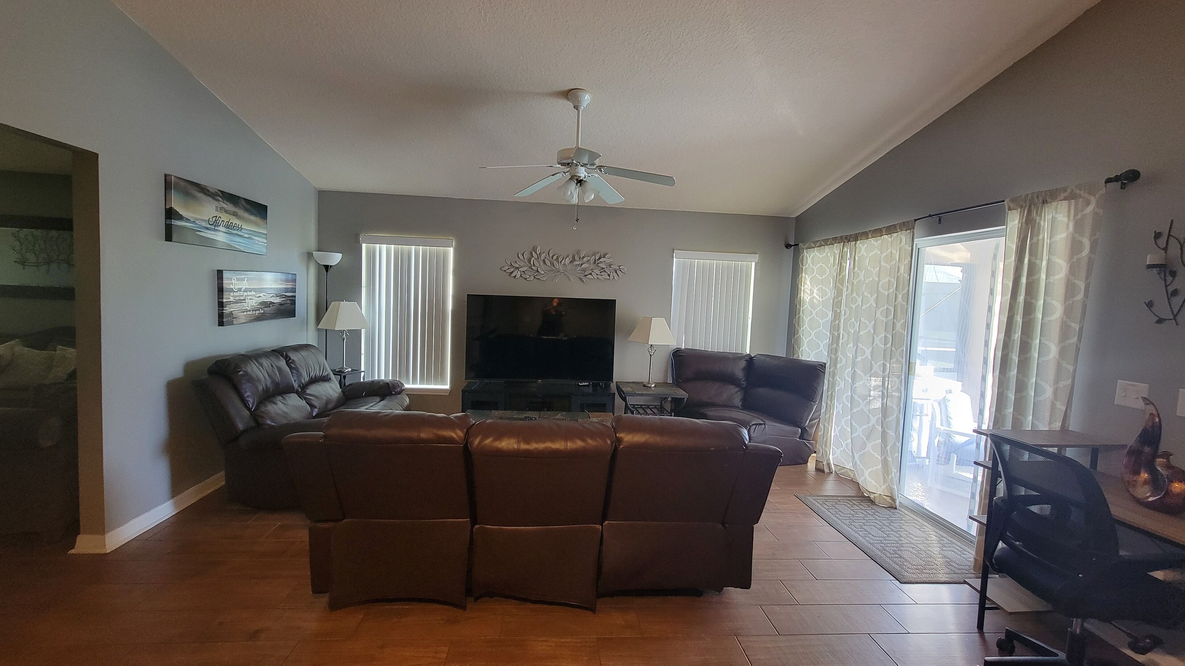 A living room with a brown leather sofa, a flat-screen TV, and a ceiling fan.