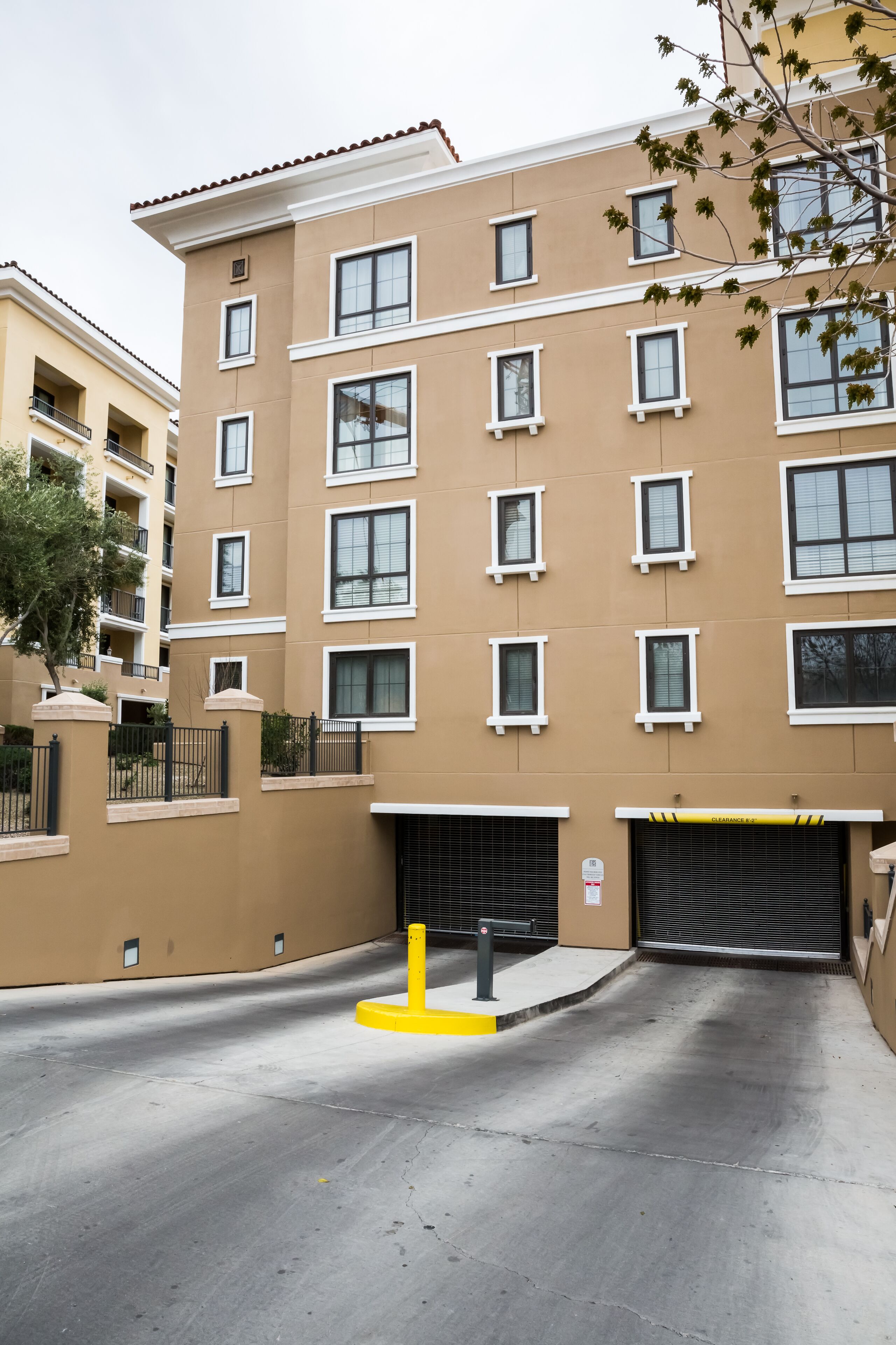 Un edificio residencial de varios pisos con fachada color beige, múltiples ventanas y acceso a un garaje.