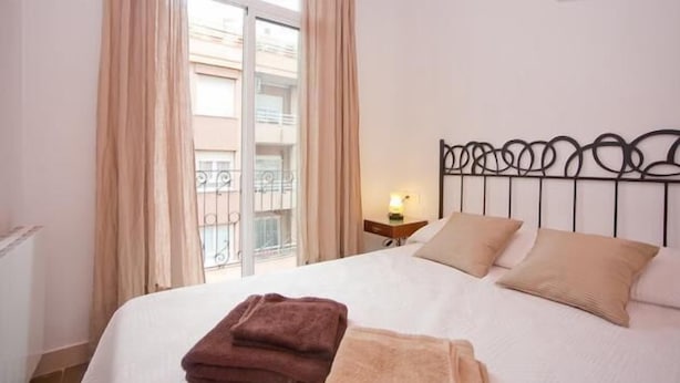 A hotel room with a bed, a nightstand, and a window with curtains. - Close Gaudi, Gracia equipped apartment, Barcelona, WIFI, balcony, AC & elevator (Barcelona)