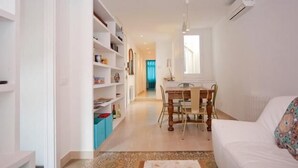 A modern living room with a white sofa, a dining table with chairs, and a bookshelf filled with books and decorative items. - Close Gaudi, Gracia equipped apartment, Barcelona, WIFI, balcony, AC & elevator (Barcelona)