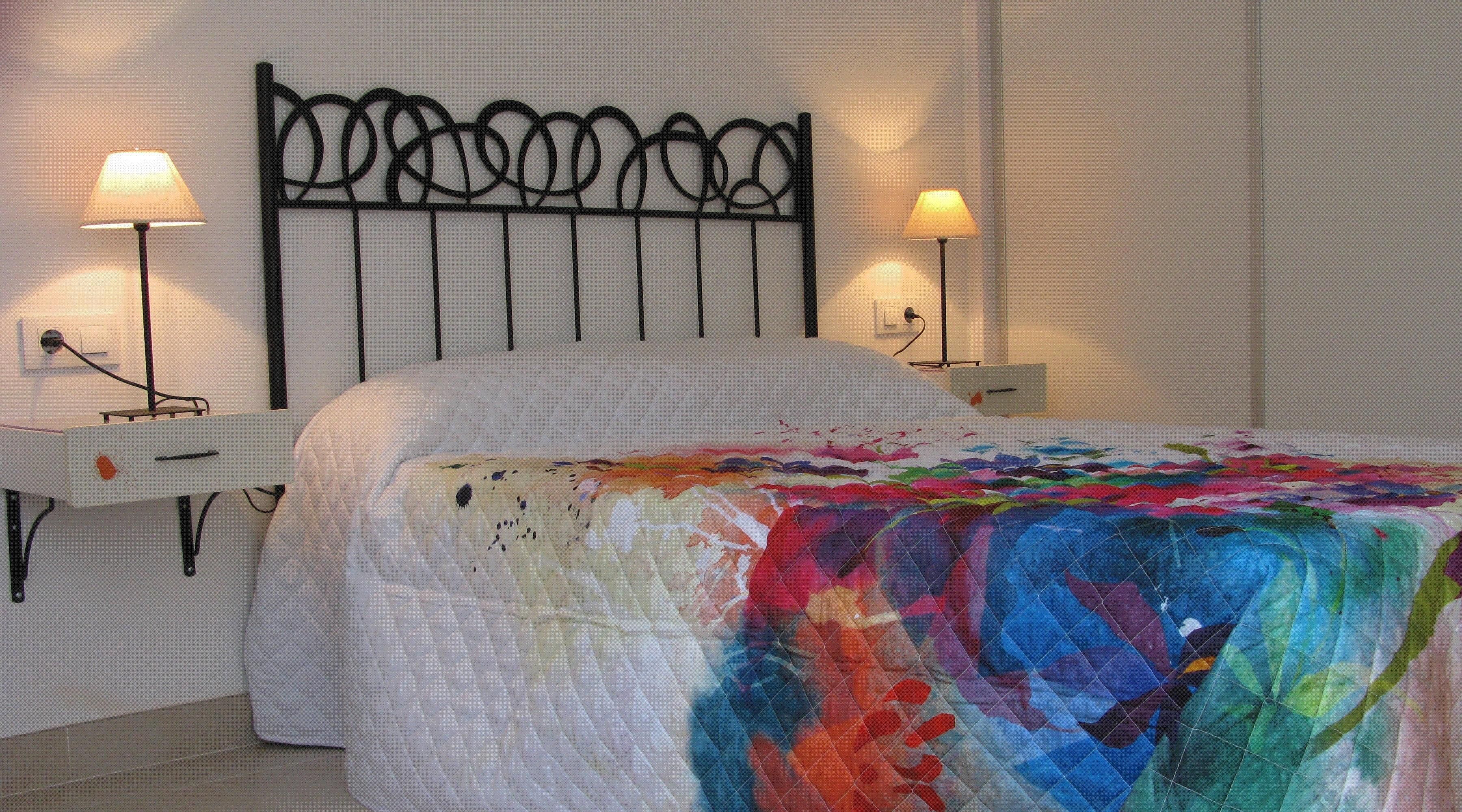 Una cama con un edredón colorido, dos lámparas de noche y un cabecero de metal negro.