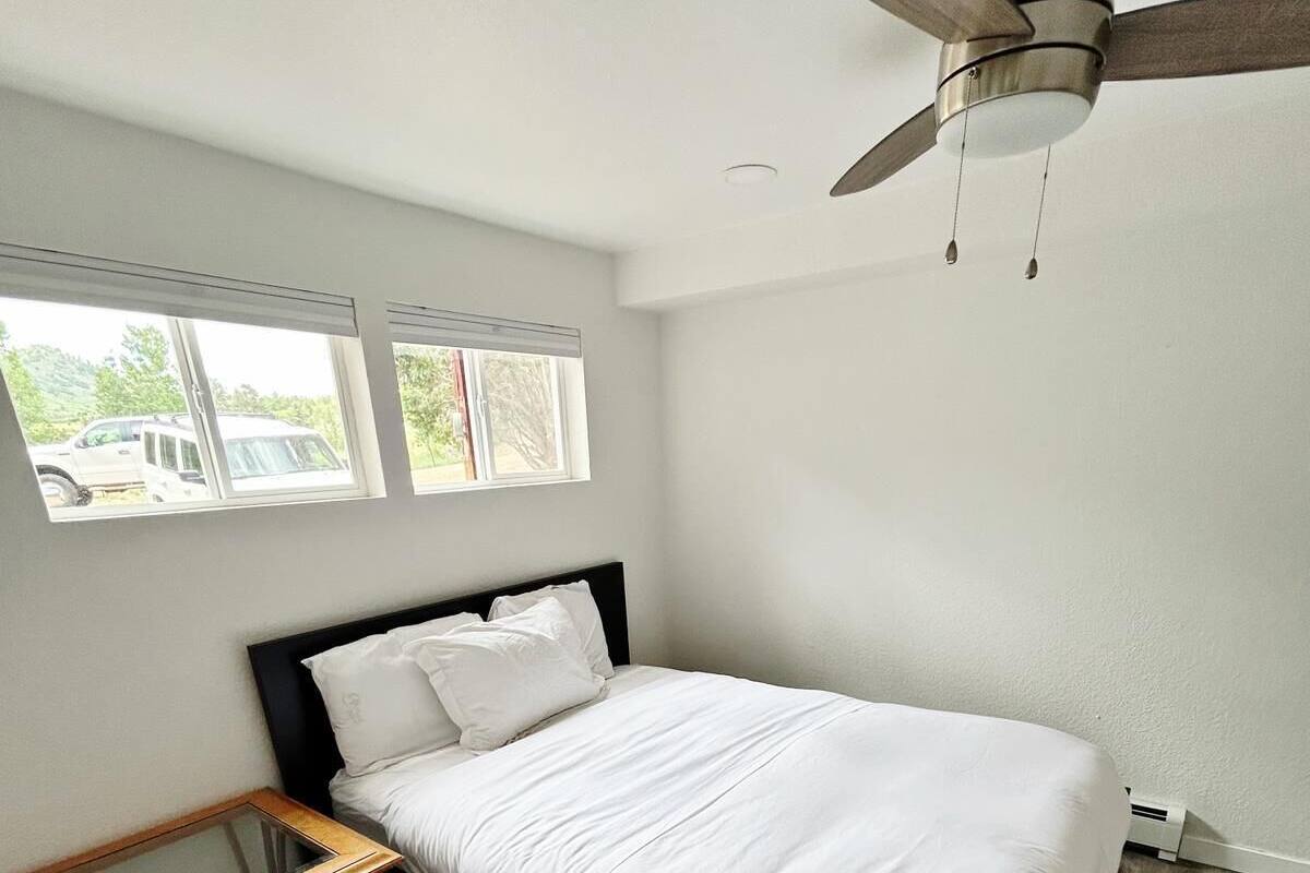 Un dormitorio con una cama, ventilador de techo, ventana y una mesa de madera.