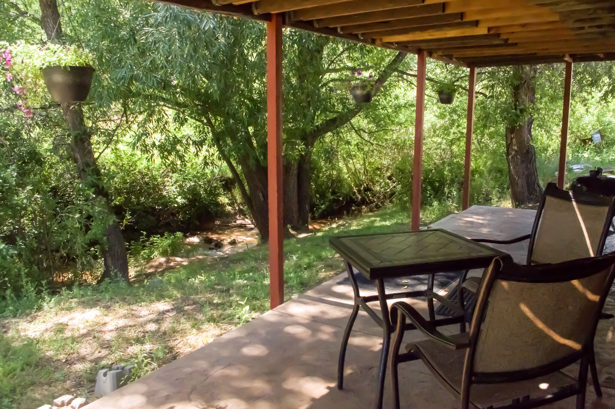 An outdoor patio with a table and chairs, surrounded by lush greenery and trees.