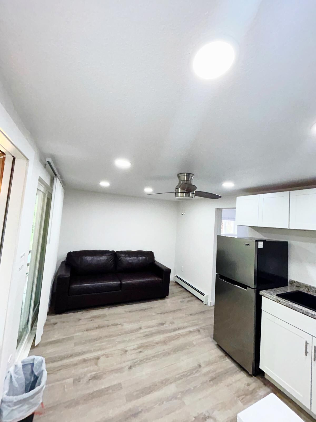 A compact living space with a kitchenette, a dark leather sofa, and a ceiling fan.