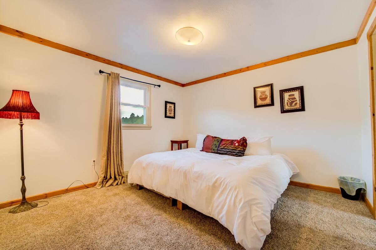 Un dormitorio con cama, una lámpara de pie, una ventana con cortinas y cuadros en la pared.
