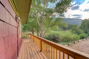 Une terrasse en bois avec une rambarde jaune, donnant sur un paysage naturel composé d’arbres et de collines.