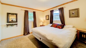 Ein Schlafzimmer mit einem großen Bett, zwei Nachttischen, einem Beistelltisch, einer Lampe, einem Spiegel und einem Fenster mit Vorhängen.