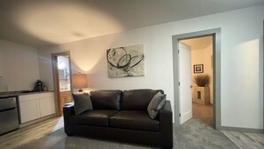 Ein Wohnzimmer mit einem dunkelbraunen Ledersofa, einem an der Wand befestigten abstrakten Gemälde und einer Tür zu einem anderen Raum.