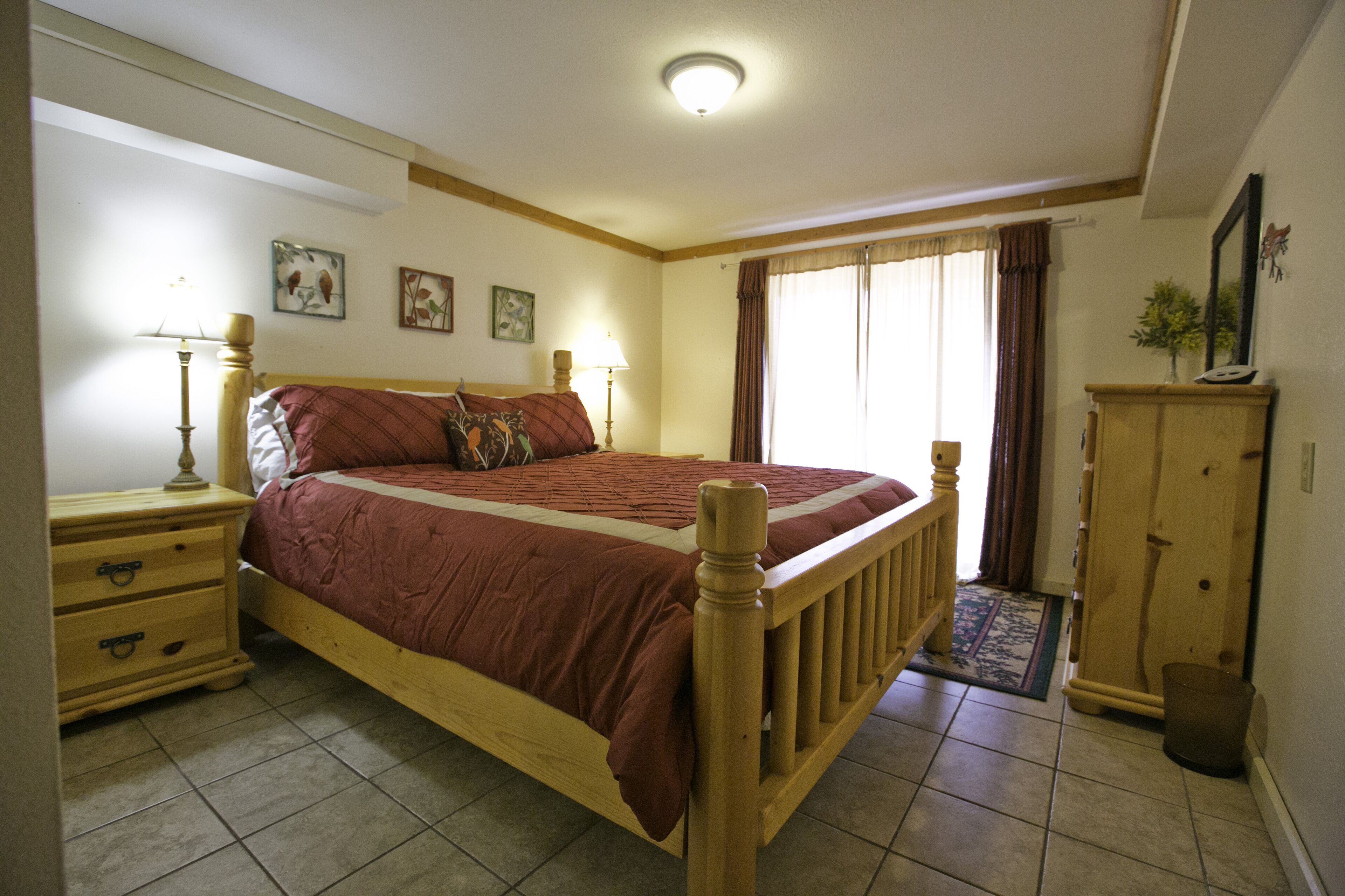Une chambre à coucher avec un lit en bois, des tables de chevet, une commode et une fenêtre avec des rideaux.