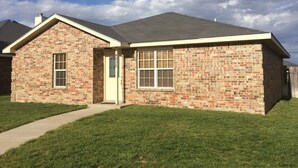 A single-story brick house with a front porch, a garage, and a well-maintained lawn.