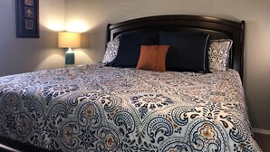 A neatly made bed with patterned bedding, a wall-mounted decorative piece, and a bedside lamp.