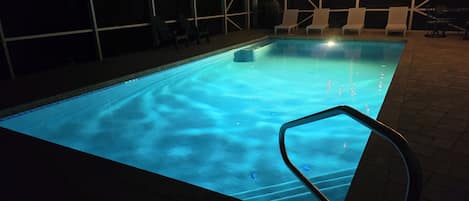 Una piscina interior con superficie de agua cristalina, rodeada de sillas de descanso y una zona de estar cubierta.